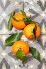 Tres mandarinas frescas con hojas en la superficie de los azulejos - foto de stock