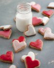 Розовое, красное и белое печенье в форме сердца со стаканом молока — стоковое фото