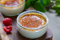 Creme brulee in glass jars with fresh raspberries on wooden board — Stock Photo