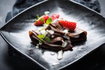 Crepes veganos de chocolate con salsa de vainilla, fresas y menta - foto de stock