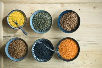 Various types of lentils in small bowls on a rustic wooden table — Stock Photo