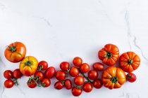 Свіжі стиглі вишневі помідори з червоним листям і зеленими гілками на білому тлі — стокове фото