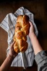 Mani con una pagnotta fatta in casa di pane intrecciato — Foto stock