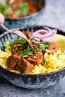 Mano con tenedor sobre el curry de ternera con arroz azafrán - foto de stock