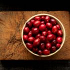Cranberries in bowl on wooden cutting board — Stock Photo