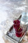 Beetroot gin in glasses with ice and thyme on metal tray with jug of cold water — Stock Photo