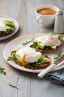 Toast con avocado, rucola e uova in camicia, caffè, foglie di rucola — Foto stock