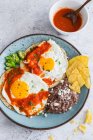 Fried eggs with tomato sauce, green chili, nachos and beans mash — Stock Photo