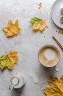 Cappuccino con un corazón de espuma de leche rodeado de hojas de otoño - foto de stock