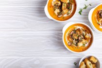 Three white ceramic bowls with pumpkin cream soup puree with mushrooms, croutons and heavy cream — Stock Photo