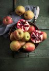 Яблоки, груши и гранат в миске на зеленой деревянной поверхности — стоковое фото