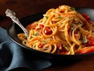 Spaghetti con pomodoro ed erbe aromatiche in ciotola nera con forchetta — Foto stock