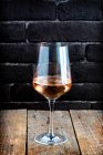 Ein einziges Glas Rosenwein auf rustikalem Holz mit schwarzem Backsteinhintergrund — Stockfoto