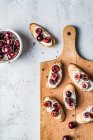 Bruschetta slices with cherries, mascarpone cream and thyme on wooden board and fresh berries in bowl — Stock Photo
