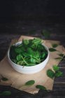 Свіже зелене листя шпинату в мисці на дерев'яному фоні. вибірковий фокус . — стокове фото