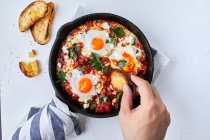 Shakshuka con tomates, pimientos, cebollas y huevos preparados en sartén de hierro fundido - foto de stock