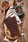 Bars of chocolate, cacao powder and cacao beans on wooden board — Stock Photo