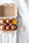 Œufs dans une boîte à œufs, une fissurée ouverte, vue sur le dessus — Photo de stock