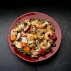 Pesce mediterraneo, vino bianco, gamberetti, cozze, vongole, calamari, pomodori in piatto su nero — Foto stock