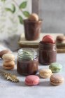 Chocolate mousse in jars with colorful macarons — Stock Photo