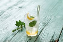 Limoncello tonic with lime zest, mint leaves and straws on wooden surface — Stock Photo
