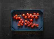 Tomates de cereja em videiras em uma caixa de madeira — Fotografia de Stock