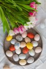 Œufs de Pâques colorés dans une assiette avec un bouquet de tulipes — Photo de stock