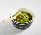 Green Matcha tea powder in bowl with wooden spoon — Stock Photo