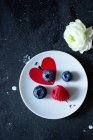 Framboises et bleuets frais sur une petite assiette avec coeur et fleur sur la table — Photo de stock