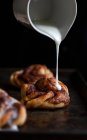 A cinnamon bun on a baking sheet being drizzled with icing — Stock Photo