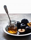 Fresh plums and honey in jar with spoon — Stock Photo