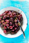 Fresh cherries in enamel bowl with knife on blue wooden surface — Stock Photo