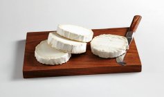 Sliced round goat's cheese with a cheese knife on kitchen board — Stock Photo