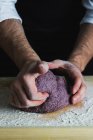 A man kneading a purple bread dough on a floured wooden surface - foto de stock