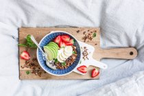 Mandeln-Sesam-Müsli mit Erdbeeren und Avocado auf Holzbrett auf dem Bett — Stockfoto