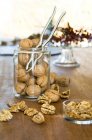 Organic walnuts, whole and cracked, in jar with nut cracker on wooden table — Stock Photo