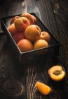 Aprikosen im Drahtkorb und auf Holztisch — Stockfoto
