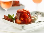 Клубничное желе со свежими ломтиками ягод, мятой и сливками на тарелке — стоковое фото