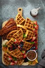 Big bar waffle café da manhã servido em uma tábua de madeira com bagas, bacon e molho de chocolate — Fotografia de Stock