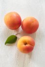 Three fresh apricots with green leaf on wooden surface — Stock Photo