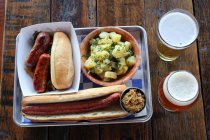 Sausages, footlong hot dog, German potato salad, stout and beer in glasses — Stock Photo