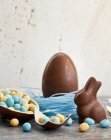 Osterschokoladenei in einem Nest mit Blaubeeren und einem Schokoladenhasen und einem halbierten Schokoladenei, das mit Mini-Schokoladeneiern gefüllt ist — Stockfoto