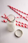 Eine kleine Flasche Milch und mehrere rote und weiße Strohhalme — Stockfoto