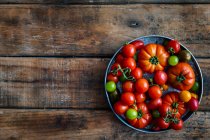Frische Tomaten in einer Schüssel auf einem hölzernen Hintergrund. Ansicht von oben. — Stockfoto