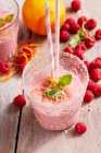 Raspberries and orange milkshakes in glasses with fresh berries and straws — Stock Photo