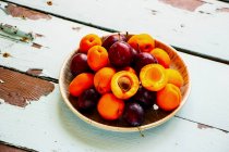 Fresh plums and apricots in wooden bowl on rustic table surface — Stock Photo