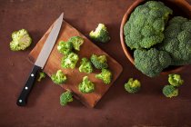 Brócolis fresco com uma faca em uma tábua de corte de madeira e em uma tigela — Fotografia de Stock