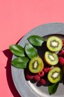 Kiwi halves with raspberries on a plate on a pink surface — Stock Photo