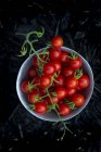 Tomates cereja frescos em uma tigela pequena na frente de um fundo escuro — Fotografia de Stock