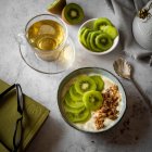Kiwi yogurt alla frutta con muesli in ambiente colazione con tè in tazza di vetro — Foto stock